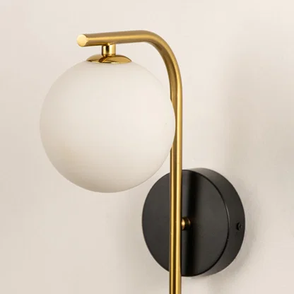 Closeup of modern wall light with frosted glass globe and gold metal arm showing smooth finish and premium design for interior decor.