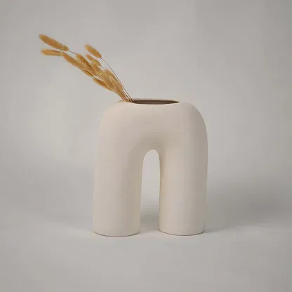Cream ceramic arch vase with a smooth sculpted form styled with dried wheat stems creating a minimal modern accent for contemporary home decor.