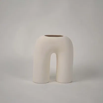 Matte cream ceramic arch vase displayed on a plain white background highlighting its sculptural form for minimal home decor accents.