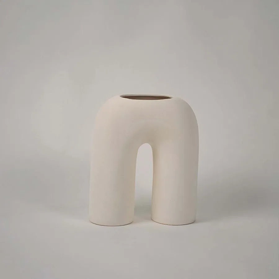 Matte cream ceramic arch vase displayed on a plain white background highlighting its sculptural form for minimal home decor accents.