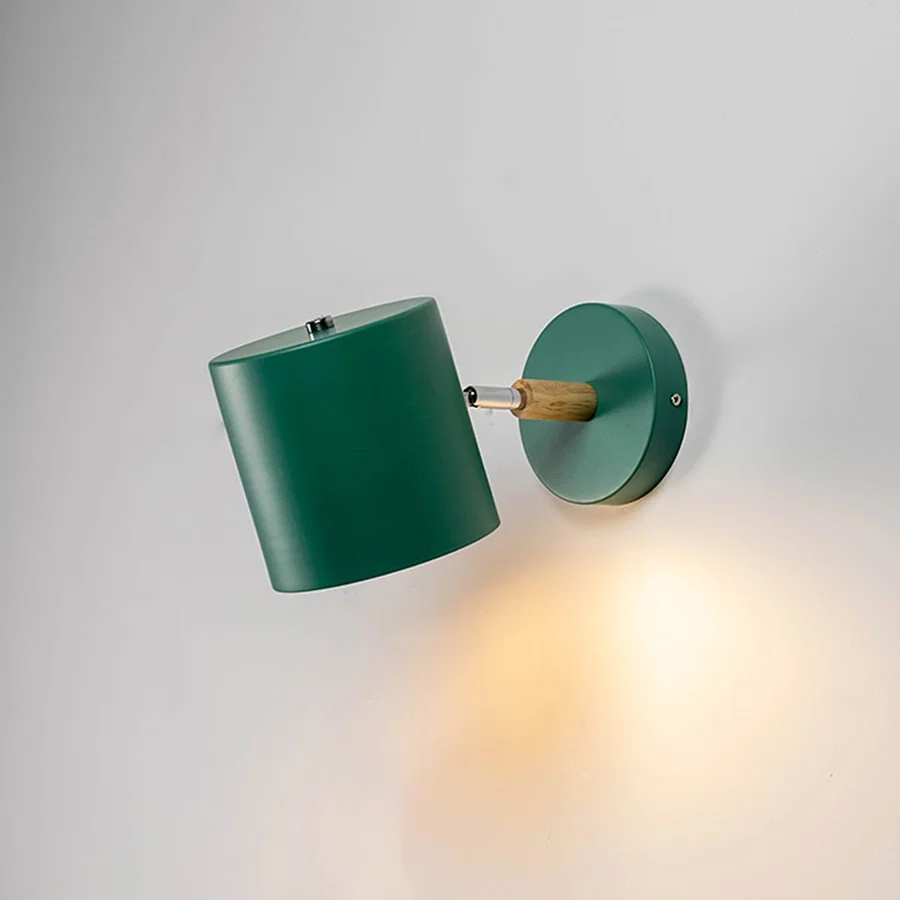 Illuminated modern green wall light with wooden detail against a plain white background highlighting the warm downward beam and material texture.