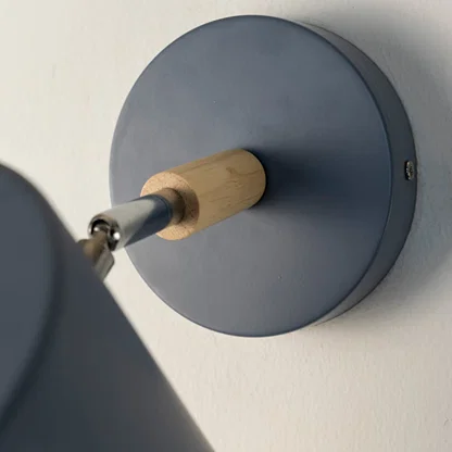 A closeup view of a blue wall lamp shows the matte texture of the shade the metallic top detail and the wooden connector giving a clear look at the craftsmanship.
