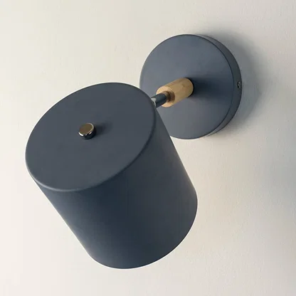 A blue wall lamp with light off is shown on a clean white background presenting its matte body wooden accent round wall plate and modern angled design.