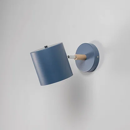 A blue wall lamp with light off is set against a grey background showcasing its matte blue shade round base and wooden connector with a strong modern silhouette.