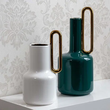 White ceramic vase with gold handle styled with coordinated decor pieces perfect for modern artistic interiors and refined decor setups.