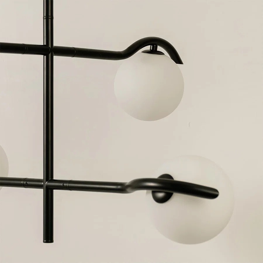 Closeup view of black metal chandelier showing curved metal arms and matte white globes for stylish modern interior lighting.