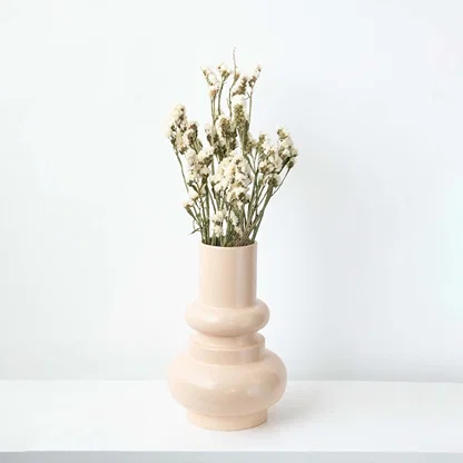 Modern peach ceramic vase placed on a white platform with patterned wall backdrop  emphasizing its elegant curves and tall silhouette.