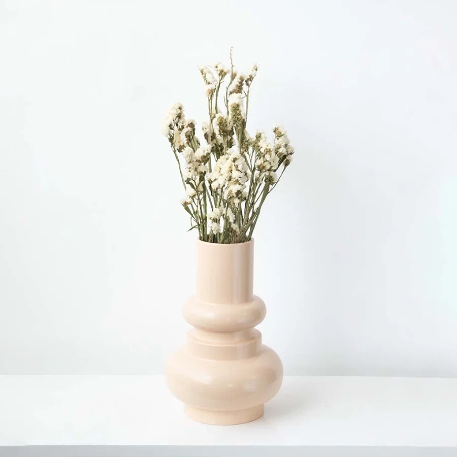 Modern peach ceramic vase placed on a white platform with patterned wall backdrop  emphasizing its elegant curves and tall silhouette.