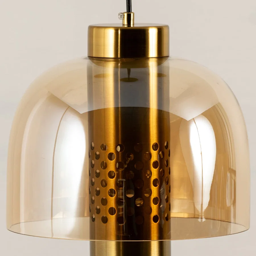 Closeup of amber glass pendant light with gold perforated metal finish for modern interior decor styling.