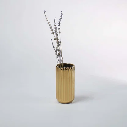 A shiny gold vase with a ribbed texture displayed in a soft minimal setting creating a warm elegant lifestyle look that highlights its modern charm.