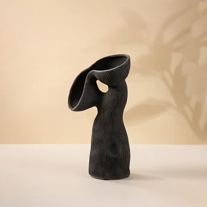 Contemporary black ceramic vase featuring unique flowing curves and ribbed surface texture on white surface.