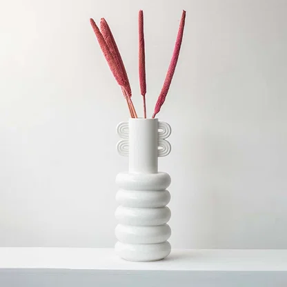 Dried grass stems in red shade styled in white ceramic vase adding artistic accent to modern tabletop home decor.