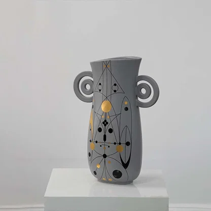 Grey ceramic vase with abstract gold and black detailing and loop handles displayed on a clean white background for modern decor styling.