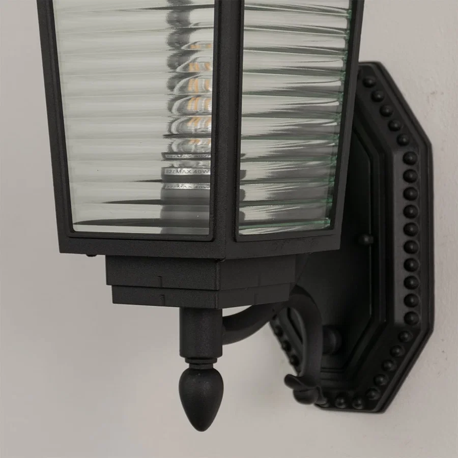 Close up view of black wall lantern showing horizontal ribbed glass detail metal frame and decorative mounting bracket design.