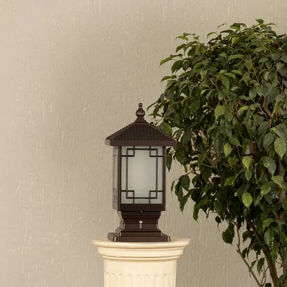 Black outdoor pillar light with ribbed glass Light On placed next to a lush green plant Lifestyle image for modern patio decor.