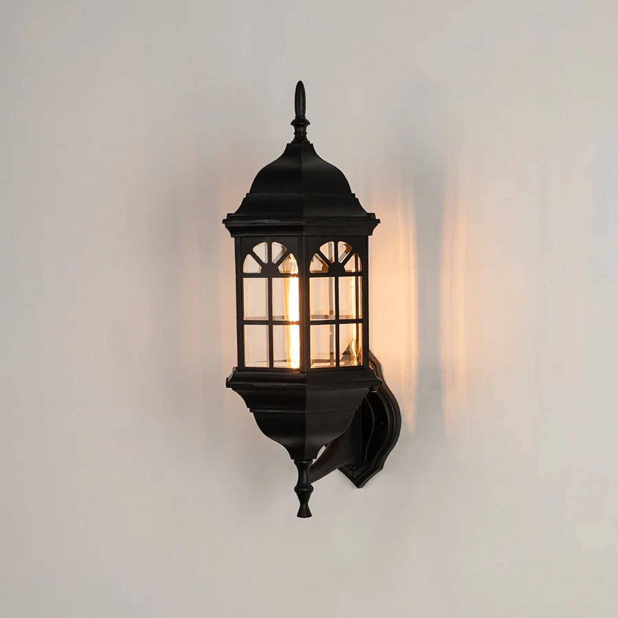 Black metal outdoor wall light on white background with an arched paneled glass shade for vintage patio decor.