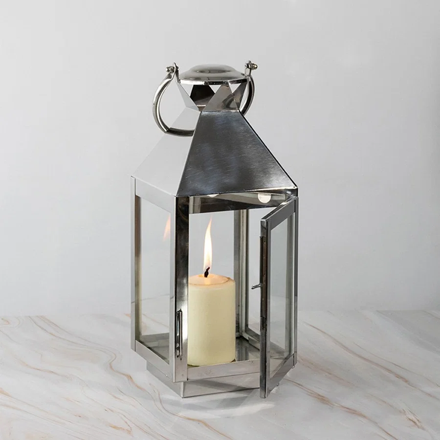 Tall stainless steel lantern with glass panels and candle lit displayed on white background for decor.