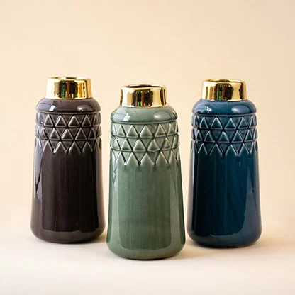 Set of three textured ceramic vases in dark grey vase green vase and blue with golden tops arranged together on a beige background creating a balanced and stylish home decor presentation.