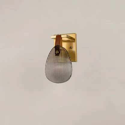 Gold metal wall sconce with ribbed glass and leather strap illuminated on white background for elegant lighting.