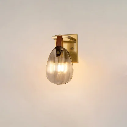 Gold wall light with ribbed glass shade and leather strap glowing on a white background for modern home lighting.