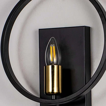 Modern wall light with circular black frame and gold holder with filament bulb on neutral background decorative lighting for interiors.