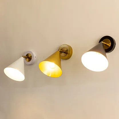 Three cone-shaped wall sconces in white gold and black finishes each lit and mounted on a light-colored wall.