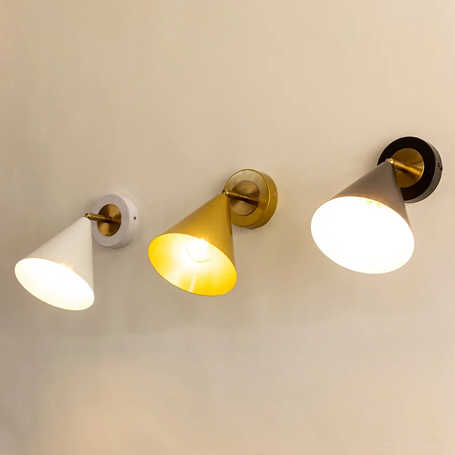 Three cone-shaped wall sconces in white gold and black finishes each lit and mounted on a light-colored wall.