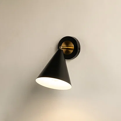 Black and gold conical wall sconce glowing softly against a clean white background showcasing modern minimalist lighting design for elegant home decor.