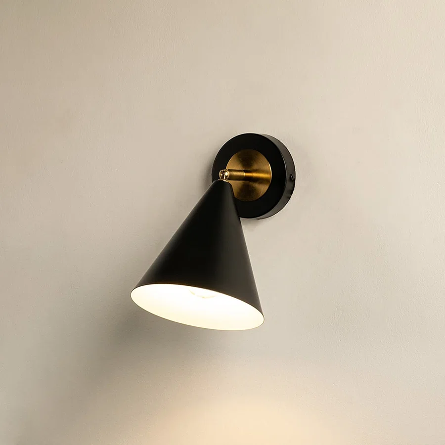Black and gold conical wall sconce glowing softly against a clean white background showcasing modern minimalist lighting design for elegant home decor.