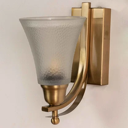 Close up view of brass wall light showing curved metal arm rectangular backplate and frosted textured glass shade details.