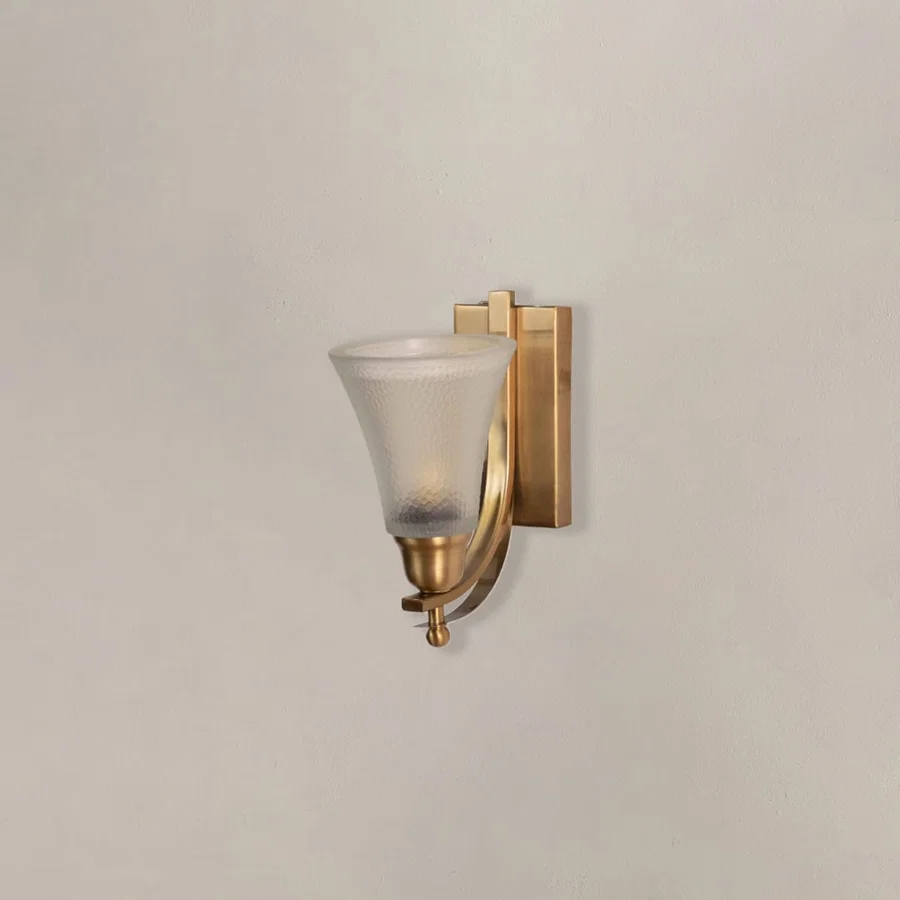 Modern brass wall lamp with frosted glass shade and curved bracket switched off displayed against dark black backdrop.
