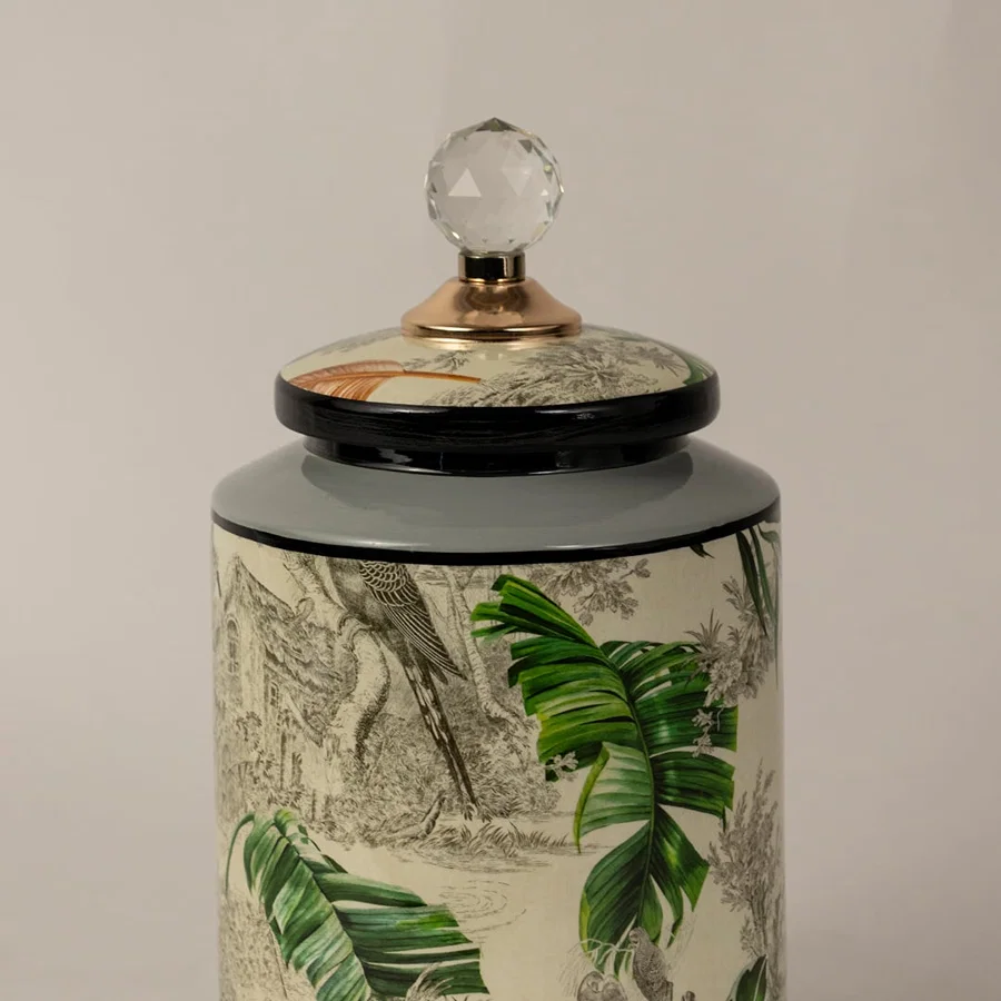 Closeup of tropical bird jar showing hand-painted bird illustration vivid tropical leaves and crystal knob.