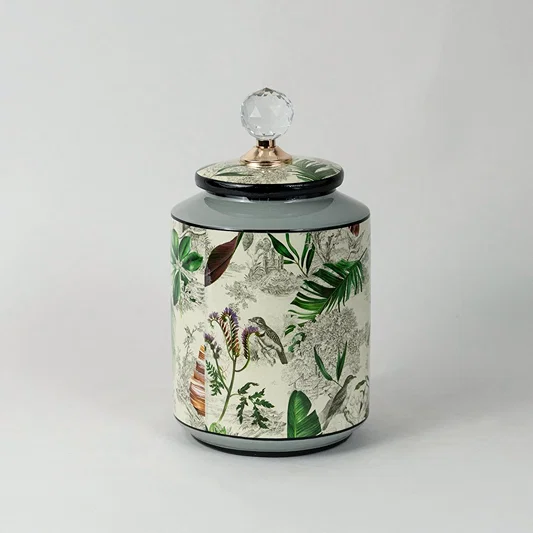Decorative ceramic jar with botanical print and glass top lid placed on white surface against neutral background showcasing stylish functional home decor accent.