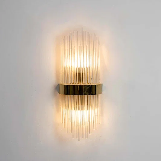 Luxury gold brass fluted glass tube wall sconce fixture illuminated brightly and isolated on a clean white background.
