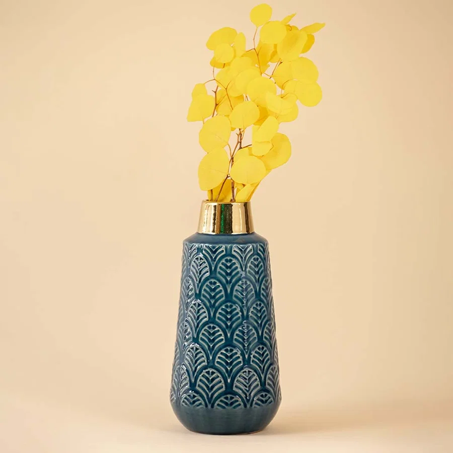 Elegant blue ceramic vase with gold detailing and textured pattern highlighted under soft neutral lighting.