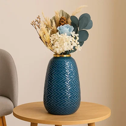 Modern blue ceramic vase with embossed zigzag design and gold top placed near a classic gold mirror in a cozy interior.