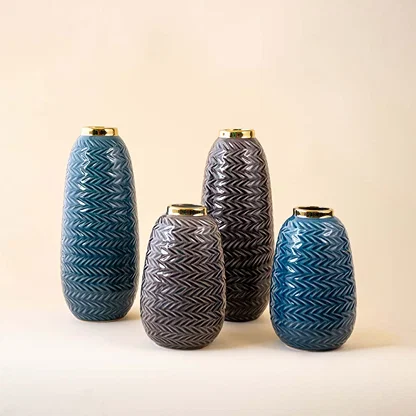 Set of grey zigzag ceramic vases with gold rims styled with coordinated floral decor in an elegant beige interior.