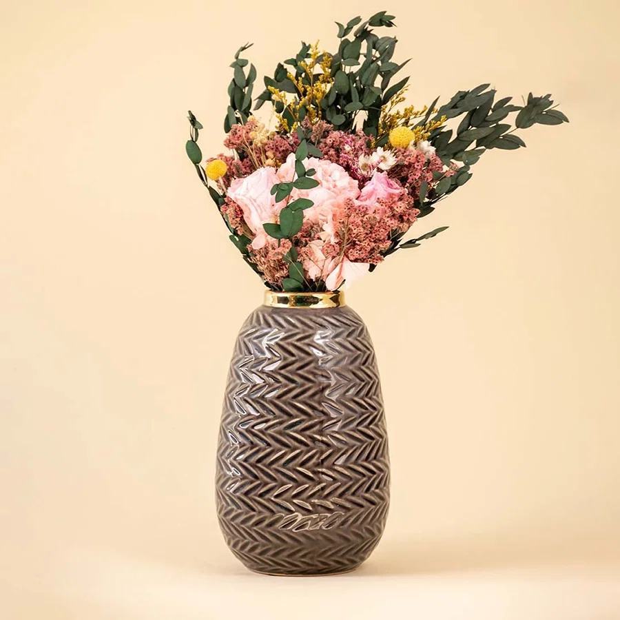 Grey zigzag ceramic vase with gold rim decorated with pink and yellow dried flowers against a beige background for elegant home decor.