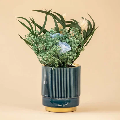 Elegant blue ceramic vase with ribbed texture and metallic gold bottom displayed with delicate flowers.