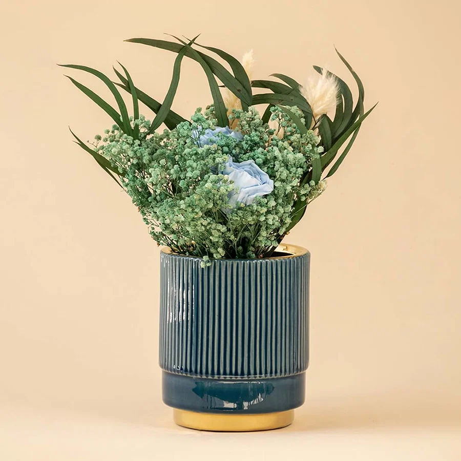 Elegant blue ceramic vase with ribbed texture and metallic gold bottom displayed with delicate flowers.
