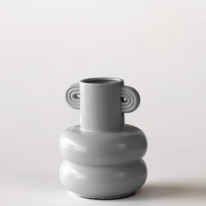 Grey sculptural vase placed on a marble surface with a warm brown backdrop creating a soft lifestyle scene.