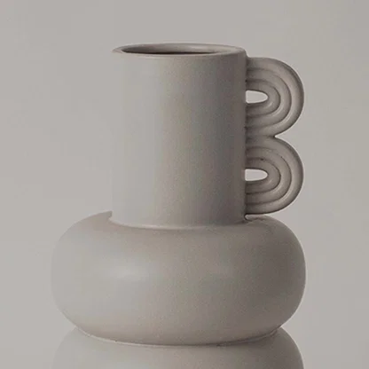 A closeup view of the sculptural neutral vase showing its smooth rounded body layered design and unique loop side detail.