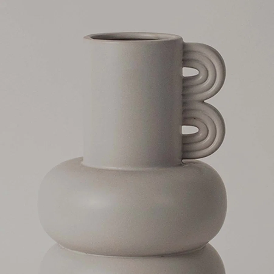A closeup view of the sculptural neutral vase showing its smooth rounded body layered design and unique loop side detail.