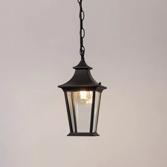 Black metal hanging lantern with clear glass glowing softly on a white background for outdoor home lighting.