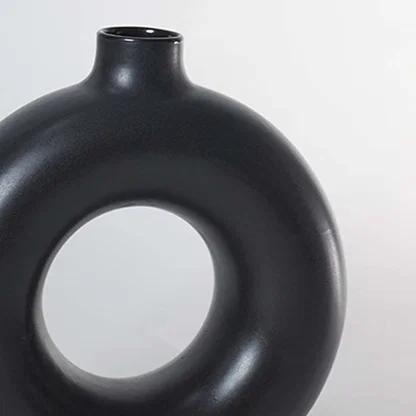 Closeup of matte black ceramic donut vase with smooth circular hollow design modern centerpiece for home decoration.