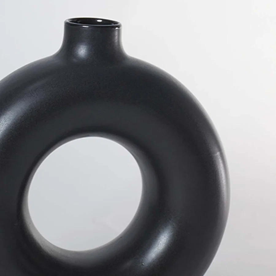 Closeup of matte black ceramic donut vase with smooth circular hollow design modern centerpiece for home decoration.