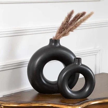 Two black circular vases displayed together on a wooden table showcasing their sculptural ring shapes and modern matte finish creating a stylish coordinated decor set.