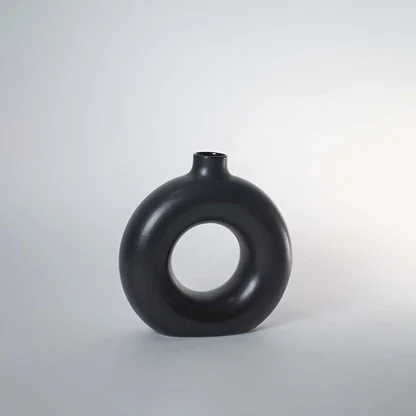 A black circular vase photographed on a white background showing its smooth rounded silhouette and central hollow design that adds a modern artistic touch to decor.