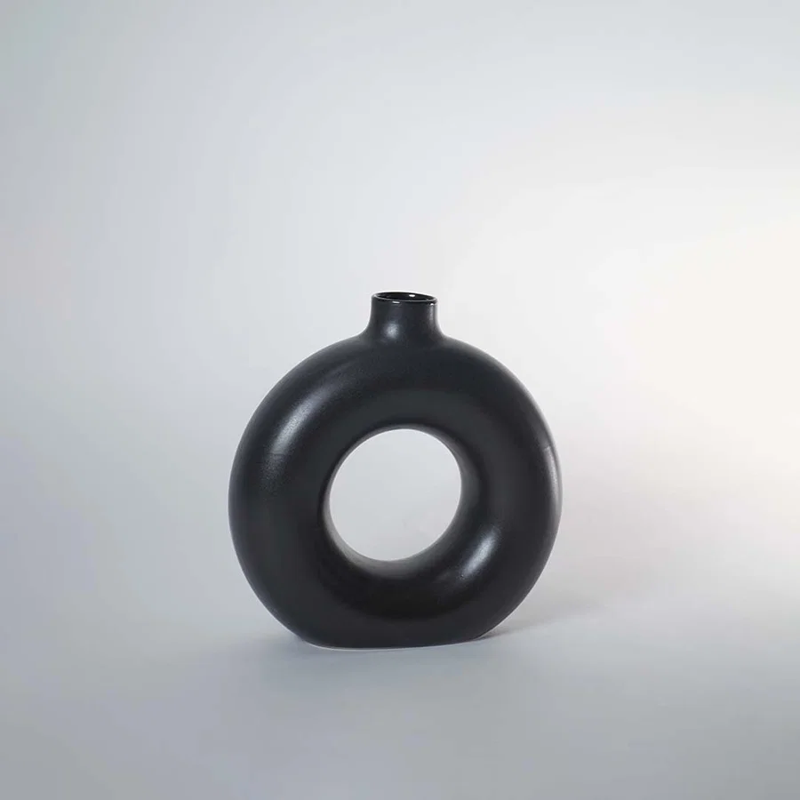 A black circular vase photographed on a white background showing its smooth rounded silhouette and central hollow design that adds a modern artistic touch to decor.