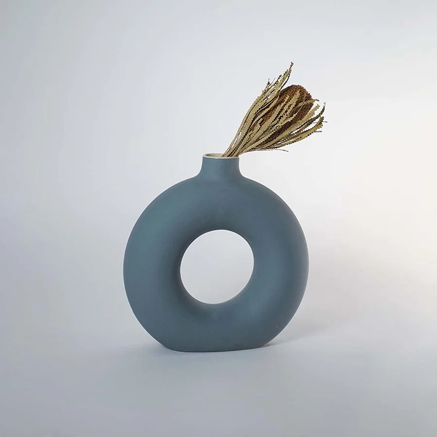 Modern green ceramic donut vase styled with dried stems placed on wooden console table for elegant home decor styling.